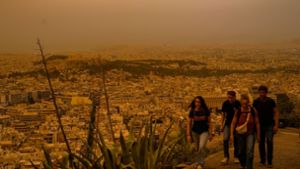 Touristen spazieren auf dem Lycabettus-Hügel in Athen, während der Himmel über der griechischen Hauptstadt mit dem antiken Akropolis-Hügel im Hintergrund infolge von Saharastaub eingetrübt ist.